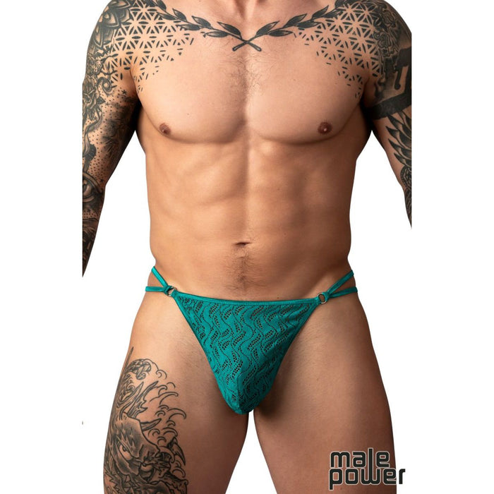 A close-up of a tattooed male model wearing a teal lace thong-style brief against a plain white background, with the Male Power logo in the bottom right corner.