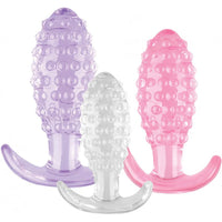 Three silicone butt plugs in purple, clear, and pink on a white background