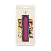 X&O's Tempt silicone rechargeable vibrator in a deep plum purple color, presented in its original cream-colored packaging with floral accents.
