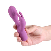 A purple silicone personal massager with a finger-like design, held in a person's hand against a plain white background.
