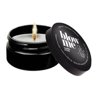 A black jar with a lid containing a lit candle, with the text 'BLOW ME' on the lid's label. The candle is labeled as a vanilla crème massage oil candle.