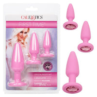 The image shows a set of three pink anal plugs with gem-adorned bases, packaged in a box with a 'First Time' branding and a model on the cover.