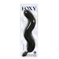 A black anal plug with a faux fur tail, packaged in a clear plastic case with the brand 'Foxy' displayed at the top.