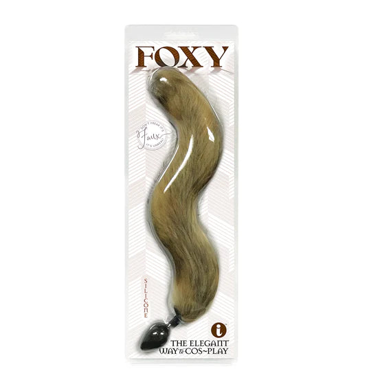 A gold anal plug with a faux fur tail, packaged in a clear plastic case with the brand 'Foxy' displayed at the top.