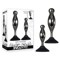 The product image shows a two-piece anal plug set with black chrome-finished alloy shapes and a suction cup base. The set is displayed alongside its packaging, which features the name 'Joy Sticks' and the brand 'Evolved'.
