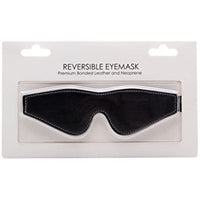 A black reversible leather eye mask presented in a clear plastic package, with the mask visible against a white background.