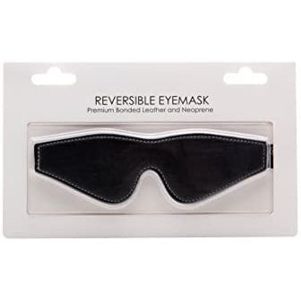 A black reversible leather eye mask presented in a clear plastic package, with the mask visible against a white background.