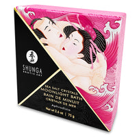 A square container of Shunga Dead Sea salt bath crystals with a graphic of a woman in a pink robe on the label. A rose and scattered bath crystals are shown in the foreground.
