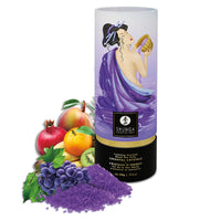 A cylindrical container of Shunga Dead Sea salt bath crystals with exotic fruit scent, accompanied by an illustration of a woman and various fruits like grapes and apples. A sea shell scoop is also shown beside the container.